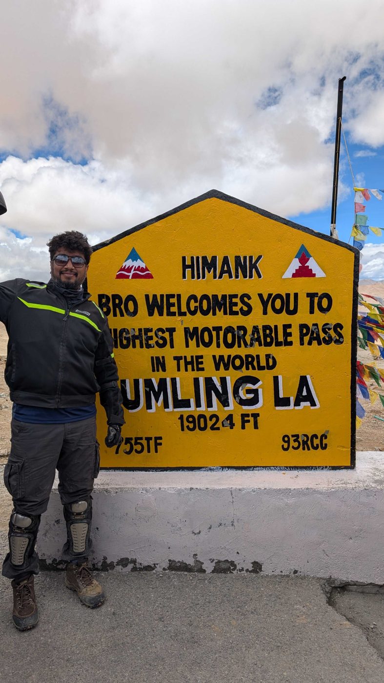 Naveen Galithoti in riding gear beside the Umling La summit sign, which reads: highest motorable pass in the world, 19,024 ft